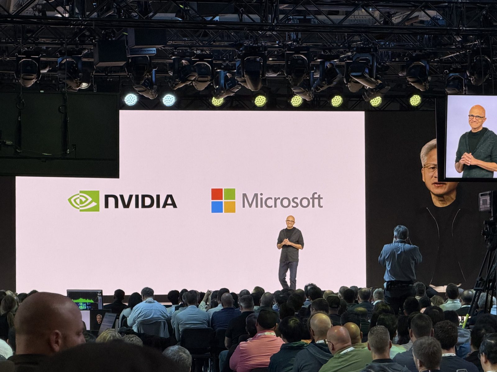 Satya Nadella on stage in front of NVIDIA and Microsoft logos, with Jensen Huang on the side screens